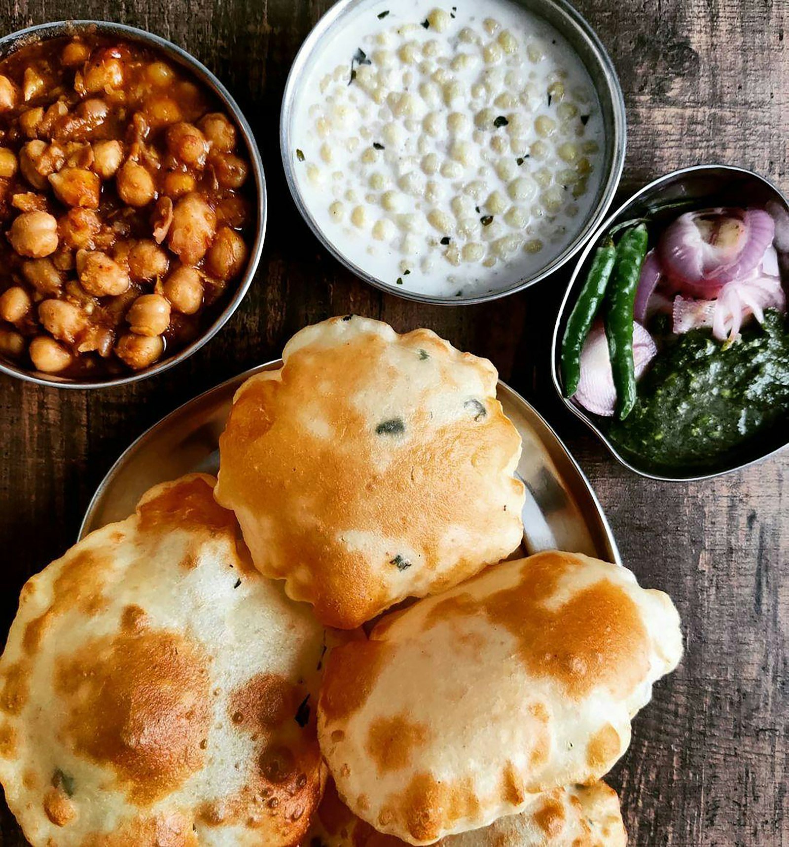 Puffed puris with a bowl of chickpea chole, raita and green chutney