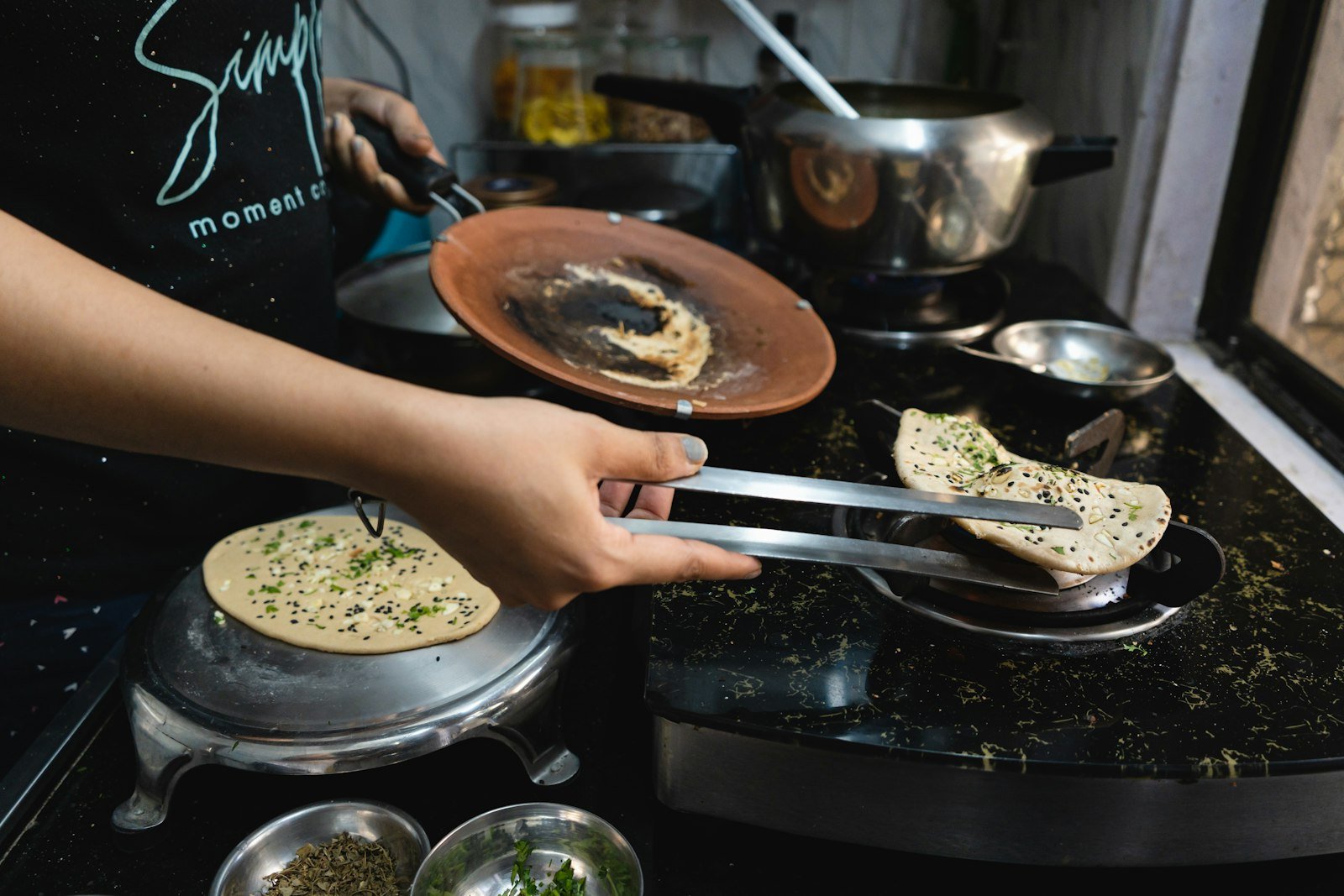 Hands using tongs to cook rotis on a tawa over a gas stove