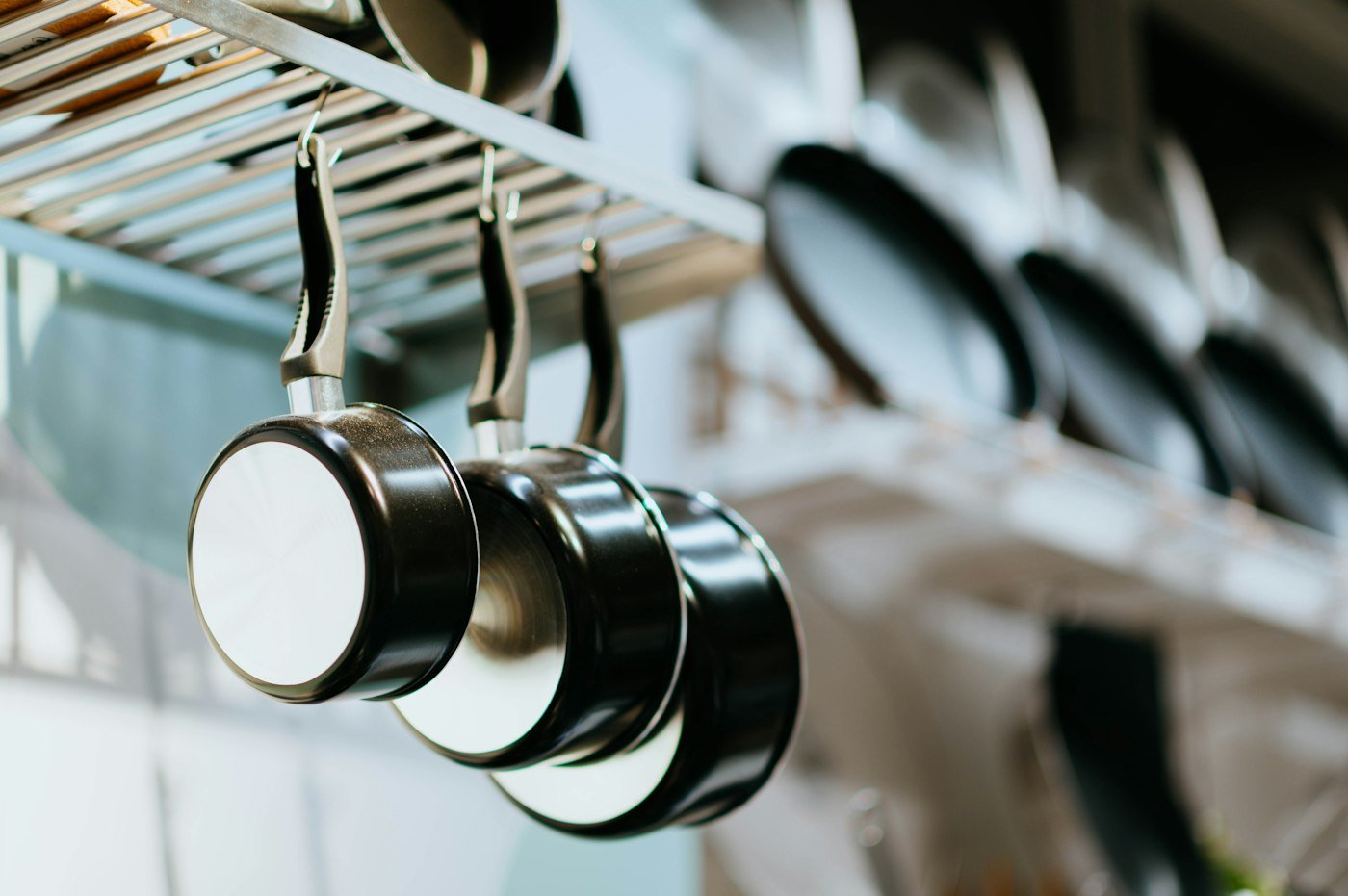Stainless steel and black frying pans hanging from a kitchen rail