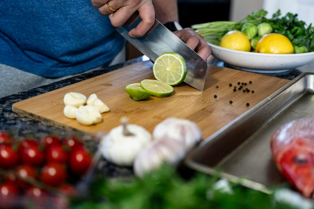 Hands cutting a lime on a wooden chopping board surrounded by tomatoes and garlic