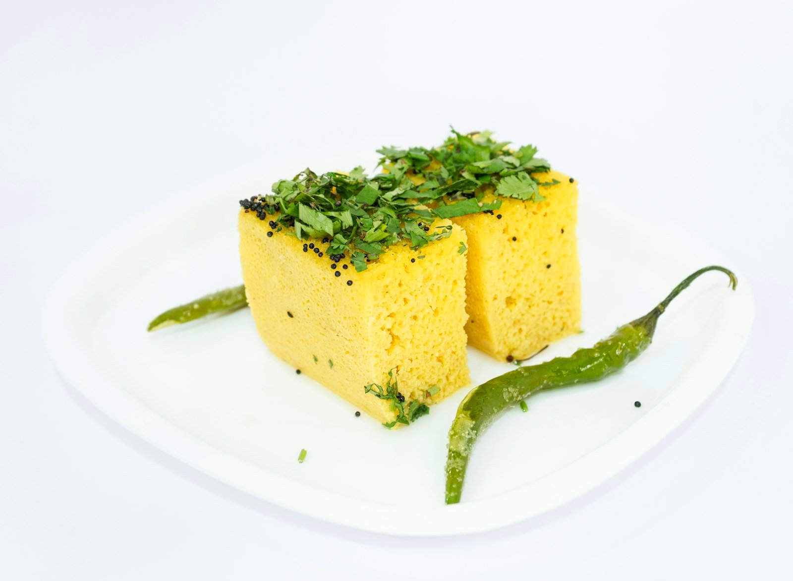 Squares of yellow khaman dhokla topped with coriander and a green chilli