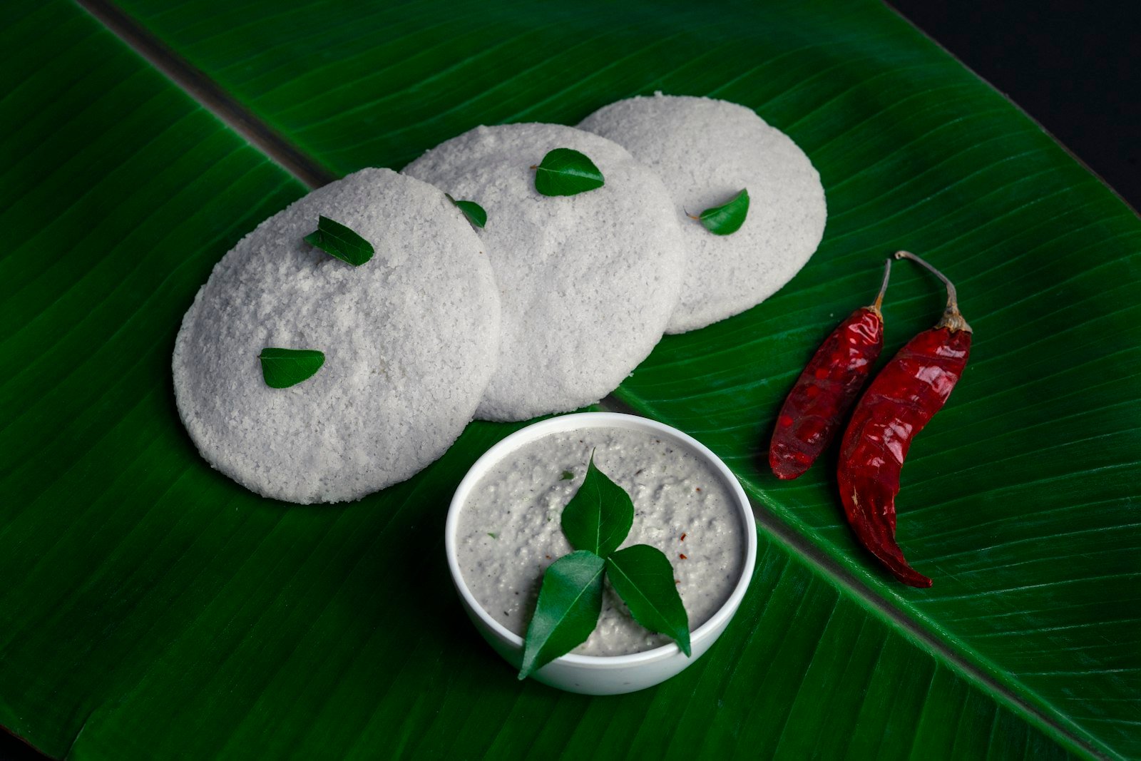 Soft idlis with coconut chutney and red chillies on a banana leaf