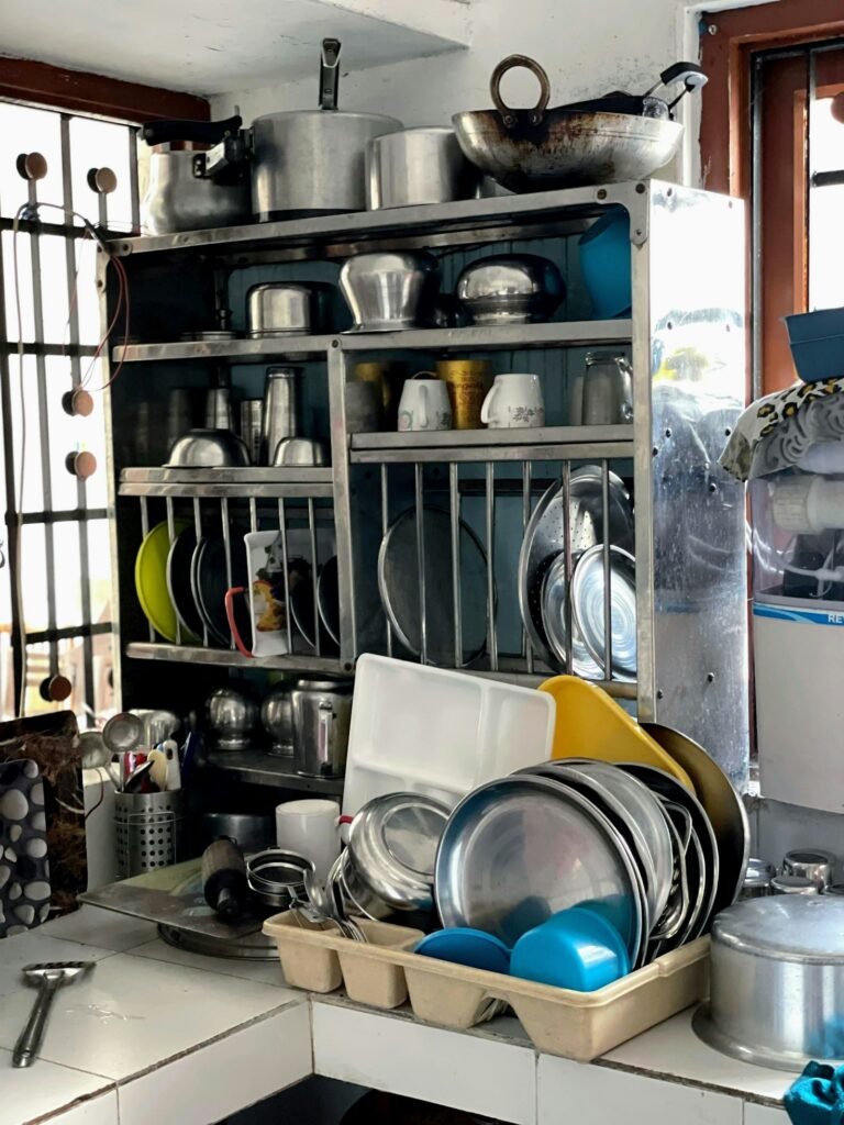 A home kitchen rack stacked with stainless steel pots, plates and utensils