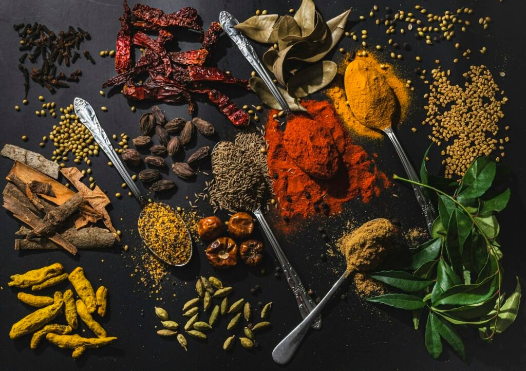 Whole and ground Indian spices with curry leaves spread across a dark surface