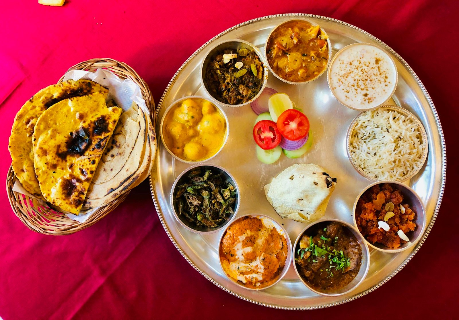 A steel thali of rotis, dal, rice and colourful vegetable dishes on a red tablecloth