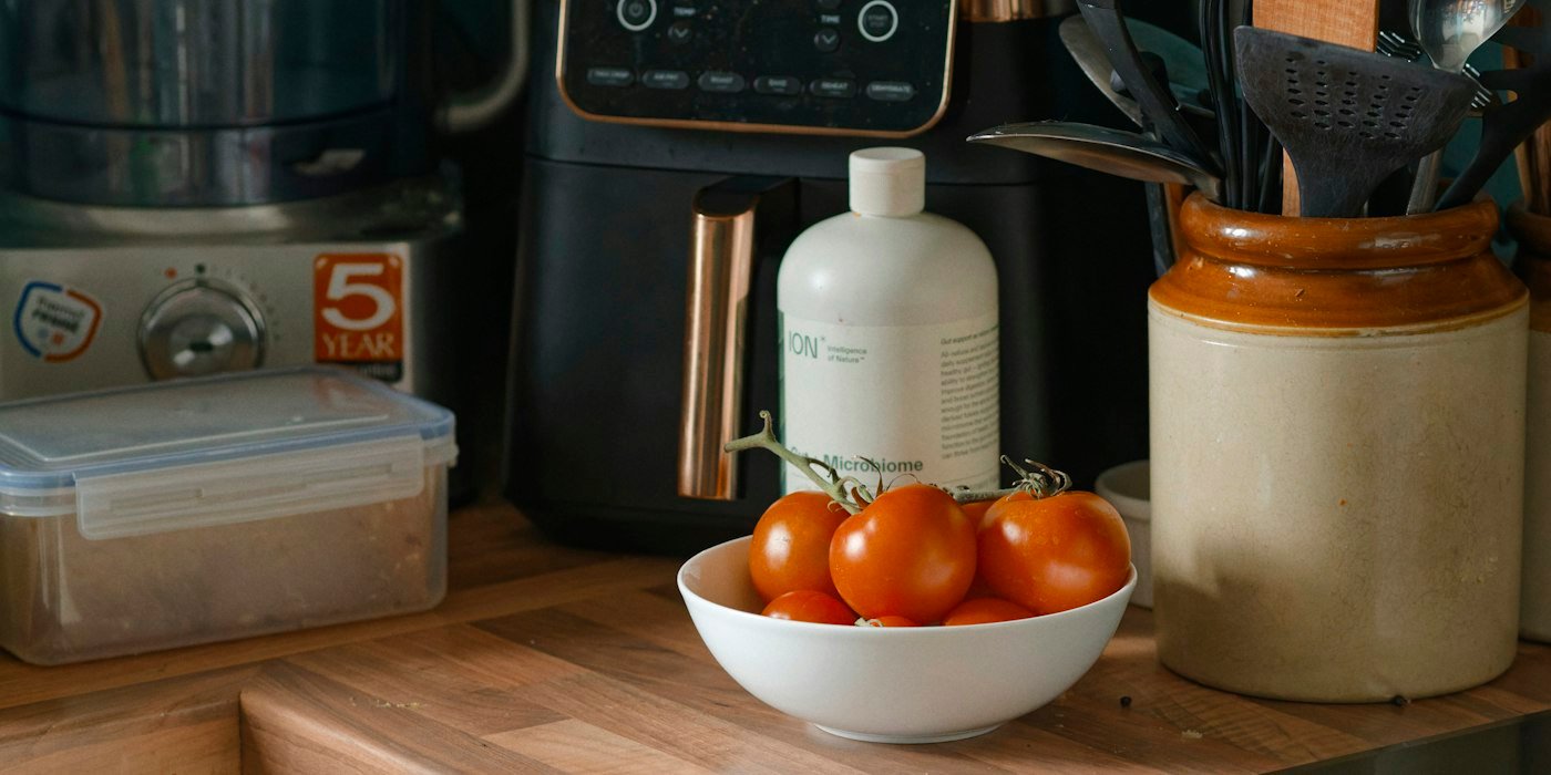 An air fryer and other small appliances on a wooden kitchen counter with a bowl of tomatoes
