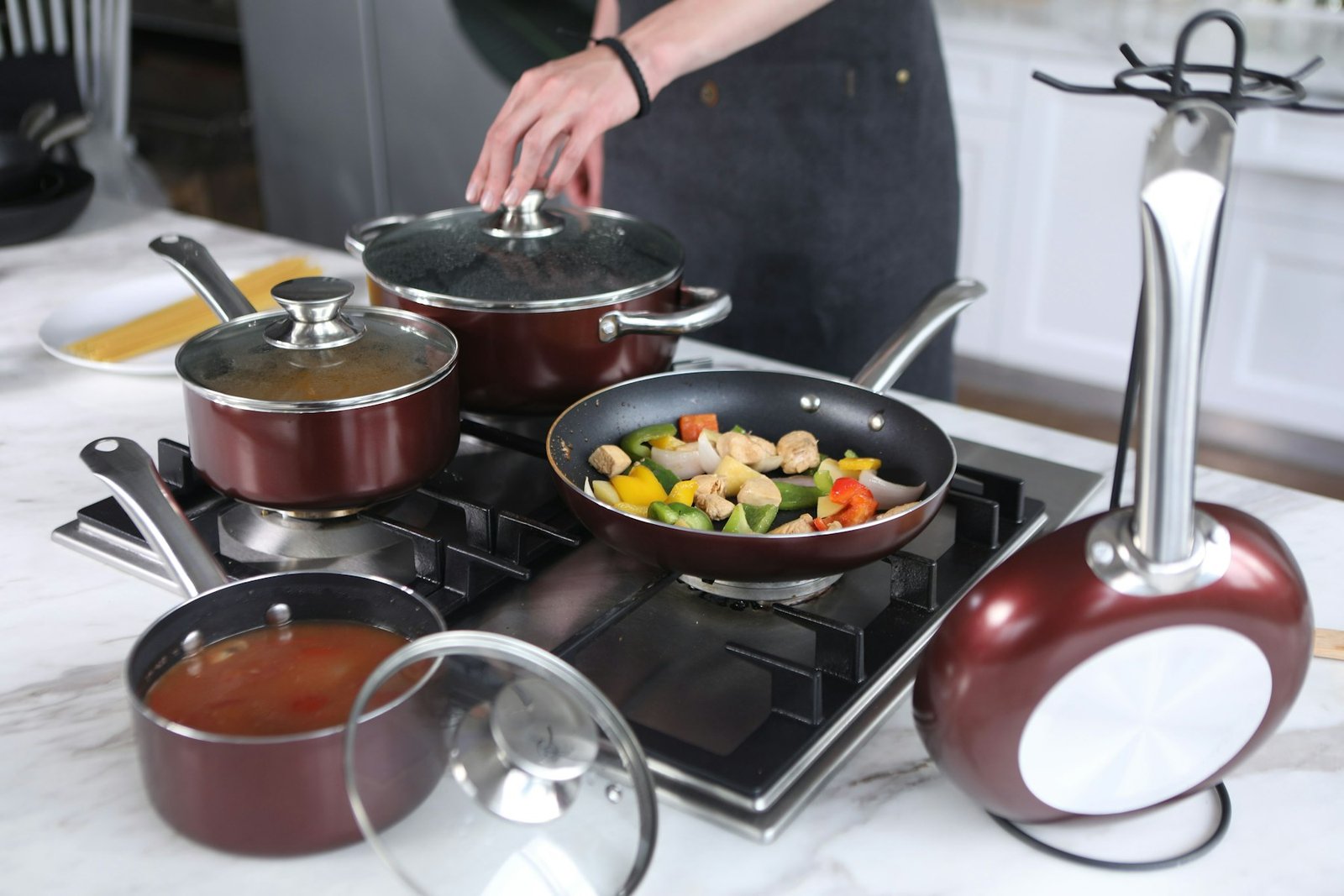 A cook stirring vegetables in a frying pan beside lidded pots on a gas stove