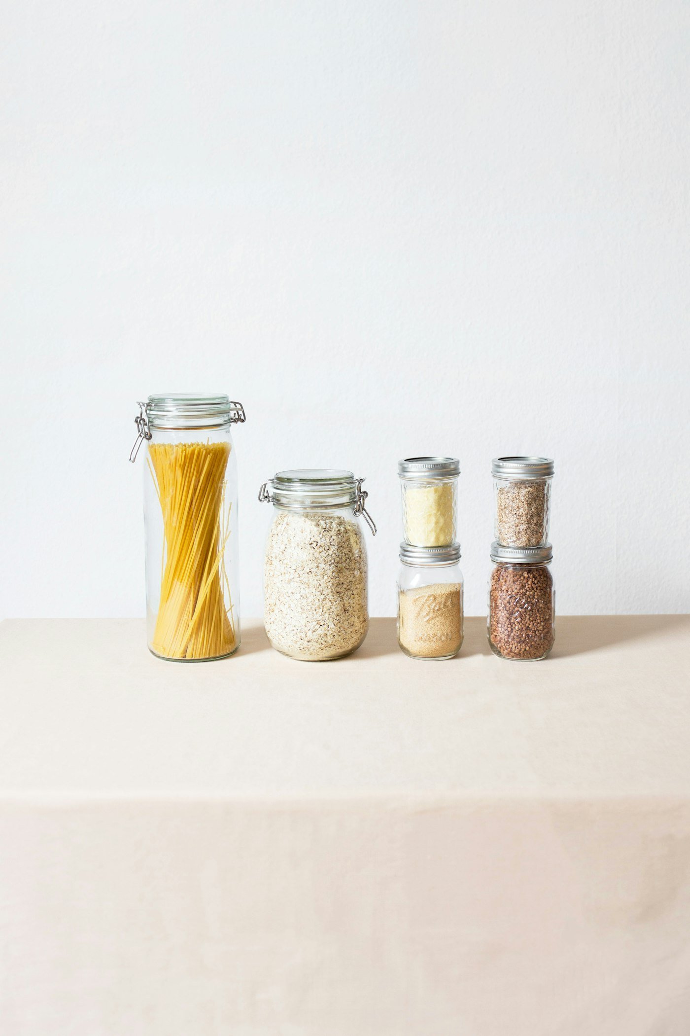Glass storage jars filled with pasta, grains and spices on a white surface