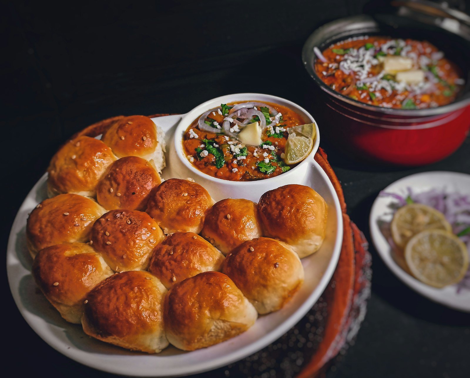 Buttered pav buns beside a bowl of spiced bhaji with onions and lemon