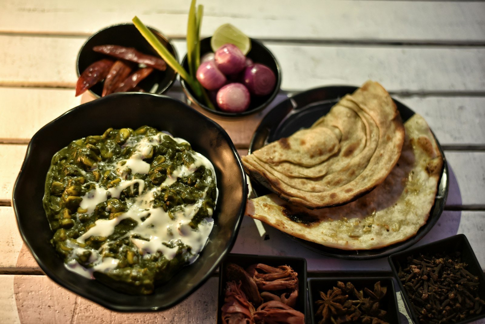 A bowl of green saag with stacked makki rotis, onions and spices