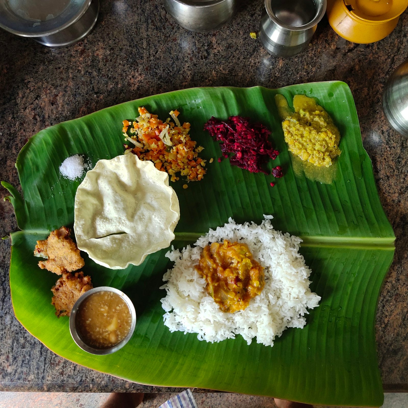 A vegetarian meal of rice, papad, curries and sides served on a banana leaf