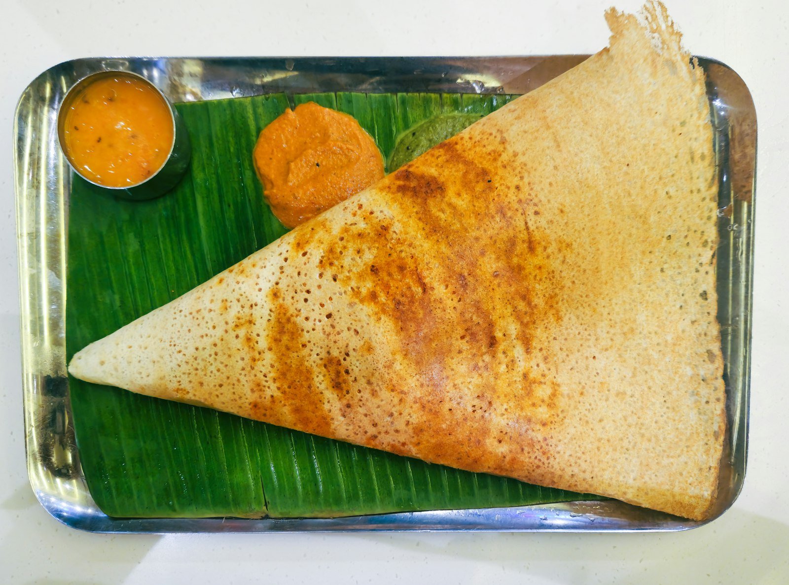 A crisp golden dosa on a banana leaf with sambar and chutneys